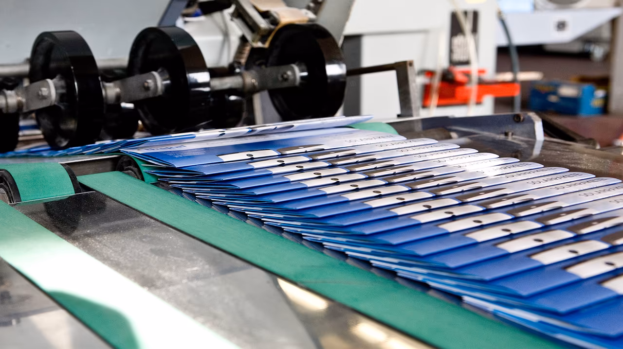 Blue printed booklets stacked on a conveyor belt in the Cal Poly Print & Copy production area.